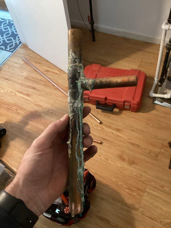Identified and repaired a pinhole leak in copper piping at corner wall junction that was causing significant water damage and pipe corrosion. Removed deteriorated section of copper pipe showing extensive greenish oxidation and replaced affected plumbing components to resolve persistent leak that was previously misdiagnosed.