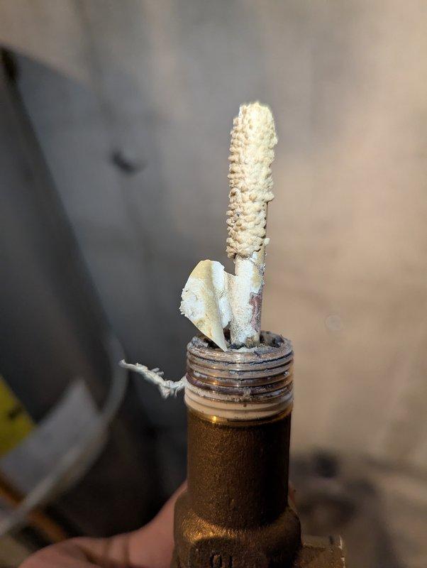 Responded to service call for a 5-year-old Rheem water heater with significant leakage from copper pipe. Diagnostic inspection revealed severe mineral buildup and corrosion at the threaded brass fitting connection, with calcified deposits extending from the connection point. Documented evidence of hard water damage contributing to the failure of the plumbing component.