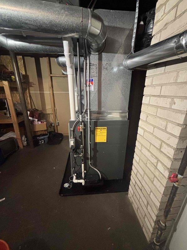 Successfully completed installation of new gray furnace unit in basement utility room, including proper connection of metal ductwork for air distribution and installation of PVC condensate drain lines. System was mounted on appropriate black platform with all warning labels properly affixed, and installation includes complete integration with existing ductwork configuration.