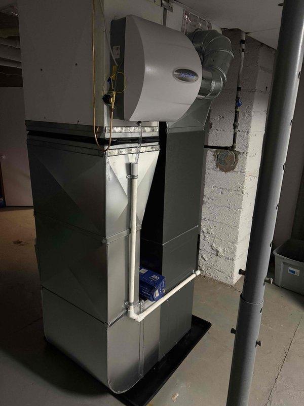 Successfully installed new Amana HVAC system including furnace with attached humidifier in utility room and outdoor condensing unit. System includes proper PVC condensate drainage, electrical connections, and all required ductwork, with the outdoor unit professionally mounted on concrete pad adjacent to home's exterior.