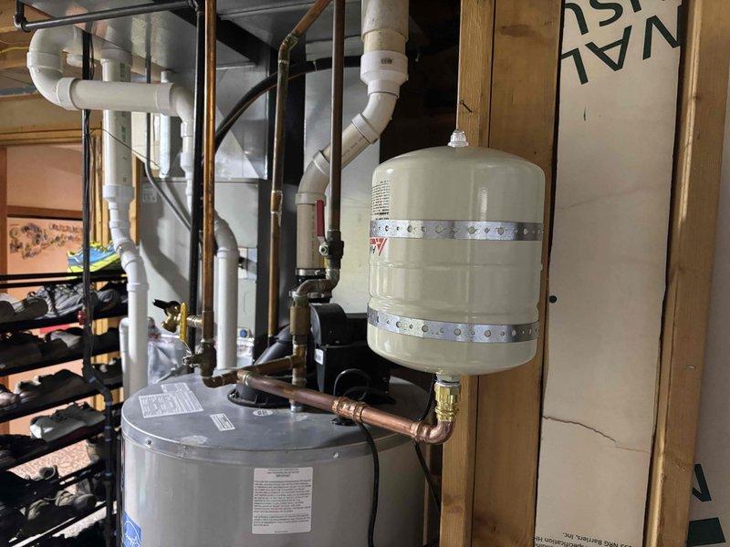 Diagnosed water heater failure and determined pressure relief valve was leaking and ignition system was non-functional. Inspected 9-year-old Goodman unit and surrounding plumbing components including the expansion tank. Documented condition of system with photos showing complete installation configuration for assessment of repair versus replacement options.