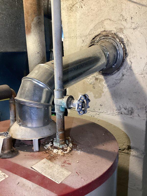 Performed comprehensive assessment of existing water heater system in basement utility room. Unit shows signs of age with corrosion at connection points, mineral buildup, and water damage/staining on adjacent wall. Documented current installation including vent pipe, pressure relief valves, and supply connections to provide appropriate replacement options.
