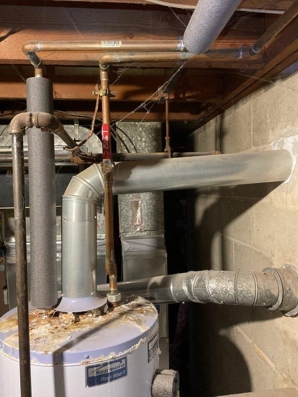 Performed annual heating maintenance on 7-year-old Goodman furnace. Observed significant corrosion and mineral buildup on water heater with deterioration of outer casing. Noted rust accumulation on water heater top surface and cobwebs throughout ductwork, suggesting ventilation system requires attention.