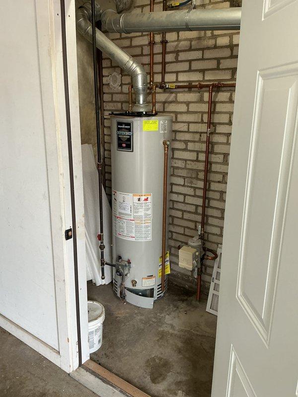 Conducted an assessment of an aging water heater system scheduled for replacement by 2026. Inspection revealed a professionally installed unit with proper copper supply line connections and appropriate metal ductwork ventilation system mounted against a brick wall in a utility area. Documented the existing installation with detailed photos to support future replacement planning.