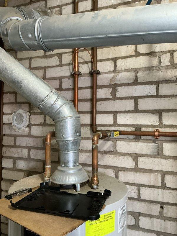 Conducted an assessment of an aging water heater system scheduled for replacement by 2026. Inspection revealed a professionally installed unit with proper copper supply line connections and appropriate metal ductwork ventilation system mounted against a brick wall in a utility area. Documented the existing installation with detailed photos to support future replacement planning.