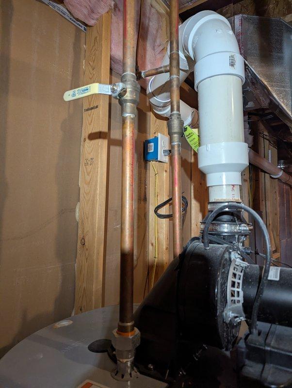 # Water Leak Service Report

Responded to water leak emergency in basement involving water heater and sump pump system. Upon inspection, identified active leaking from water heater plumbing connections and sump pump assembly. Water heater exhibited leakage at copper pipe connections near the white PVC discharge piping system, with visible moisture accumulation around aged copper fittings. Sump pump showed signs of leakage at the pump housing and discharge connection points, with the black cylindrical pump motor assembly displaying water intrusion.

Performed comprehensive assessment of all plumbing connections, pipe integrity, and mechanical equipment in the affected basement utility area. Documented existing conditions through photographic evidence showing the full extent of the water intrusion and equipment layout, including exposed framing, insulation, and mechanical systems. Identified compromised connections requiring immediate attention to prevent further water damage to the unfi