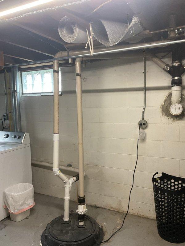 # Service Report

Completed inspection and documentation of existing basement plumbing and radon mitigation systems. The radon mitigation system features a white PVC vertical pipe configuration with proper floor penetration and ceiling routing through the utility area. Under-sink plumbing was inspected, including a black garbage disposal unit with white PVC drainage piping and chrome P-trap assembly in proper working configuration. All visible plumbing connections, drainage systems, and utility installations were photographed for record-keeping purposes. The laundry area plumbing and associated mechanical systems were confirmed to be accessible and properly installed per standard residential specifications.