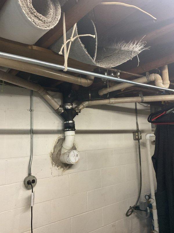 # Service Report

Completed inspection and documentation of existing basement plumbing and radon mitigation systems. The radon mitigation system features a white PVC vertical pipe configuration with proper floor penetration and ceiling routing through the utility area. Under-sink plumbing was inspected, including a black garbage disposal unit with white PVC drainage piping and chrome P-trap assembly in proper working configuration. All visible plumbing connections, drainage systems, and utility installations were photographed for record-keeping purposes. The laundry area plumbing and associated mechanical systems were confirmed to be accessible and properly installed per standard residential specifications.