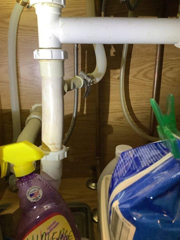 # Plumbing Leak Service Report

Responded to service call for reported water leak in basement area beneath kitchen sink, with customer noting increased moisture during rainy weather. Upon inspection, examined under-sink plumbing assembly consisting of white PVC drain pipes with P-trap configuration and flexible braided stainless steel supply lines connected to shut-off valves. Assessed all visible plumbing connections, drain assembly, and supply line fittings for signs of active leakage or moisture intrusion. Documented existing plumbing configuration with photographs showing cabinet interior, pipe connections, and overall sink installation to establish baseline conditions for repair recommendations.