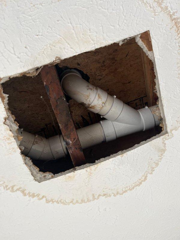 # Service Report: Toilet Leak Repair

Responded to callback for recurring toilet leak at property, two days after customer reported issue. Previous seal repair completed in early February had failed. Upon arrival, conducted thorough inspection to identify source of active leak in specific location reported by customer.

Investigation revealed compromised plumbing connections in ceiling cavity beneath toilet fixture. Accessed repair area through existing ceiling opening to examine PVC pipe configuration and joints. Found deteriorated seal at pipe connection causing water seepage into surrounding structure. Evidence of moisture damage and staining visible on ceiling surface surrounding access point.

Performed complete seal replacement at affected pipe joint using appropriate plumbing-grade sealant and compression fittings. Verified all connections were properly secured and tested system under pressure to confirm leak resolution. Documented conditions before and after repair with photogr