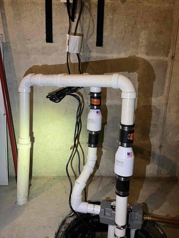 # Job Description

Responded to a sump pump and water backup emergency under a QUOTR-quoted repair authorization. Upon arrival, assessed the existing plumbing system and identified failures in the backup prevention infrastructure that were allowing water intrusion during heavy flow conditions.

Installed a comprehensive water backup prevention system consisting of dual check valve assemblies with brass fittings and shut-off valves on the main water supply line. Mounted a white filtration housing unit to the concrete wall using secure black brackets, integrating it with the existing copper supply piping. Connected all components using appropriate brass compression fittings and copper pipe extensions to ensure proper water flow and system isolation capability.

On the drainage side, configured a white PVC pipe assembly in a vertical loop configuration to manage sump discharge and prevent backflow. Integrated two electronic water backup prevention devices with American-flag-branded housin