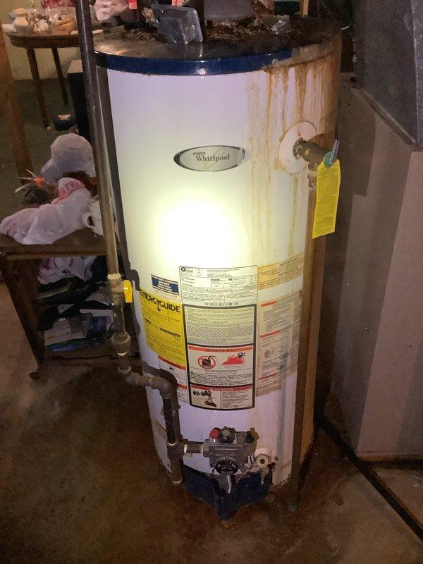 # Service Report: Water Heater Estimate

Completed comprehensive water heater evaluation for residential property. Existing Whirlpool tank-type water heater exhibits significant deterioration including extensive rust staining on exterior casing, severe corrosion at top fittings and valve connections, and visible water damage patterns indicating potential internal tank failure or chronic leakage from upper components. Unit displays advanced age-related wear compromising structural integrity and operational reliability.

Assessed existing plumbing infrastructure including supply lines, discharge piping, and overhead connections. Documented copper supply piping with foam insulation, ceiling-mounted expansion tank assembly with pressure relief components, and current venting configuration. Evaluated installation space constraints, utility connections, and code compliance requirements for replacement options.

Provided detailed estimate comparing conventional tank-type water heater replacem