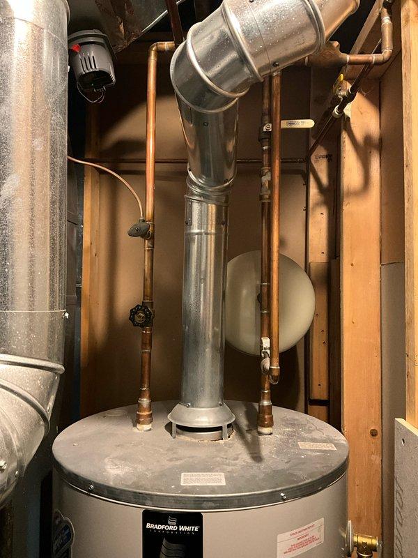 # Service Report: Water Heater Replacement Estimate

Completed on-site assessment for water heater replacement in residential utility space. Existing Bradford White water heater unit is positioned in confined area with limited clearance, located behind furnace equipment requiring partial HVAC system disassembly for proper access. Documented current installation including copper supply line connections, brass shut-off valves, galvanized flue vent system, and expansion tank mounting. Evaluated spatial constraints and confirmed furnace will need to be temporarily relocated to facilitate safe removal of old unit and installation of replacement water heater. Customer requested expedited replacement service due to immediate need.