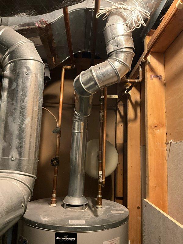 # Service Report: Water Heater Replacement Estimate

Completed on-site assessment for water heater replacement in residential utility space. Existing Bradford White water heater unit is positioned in confined area with limited clearance, located behind furnace equipment requiring partial HVAC system disassembly for proper access. Documented current installation including copper supply line connections, brass shut-off valves, galvanized flue vent system, and expansion tank mounting. Evaluated spatial constraints and confirmed furnace will need to be temporarily relocated to facilitate safe removal of old unit and installation of replacement water heater. Customer requested expedited replacement service due to immediate need.