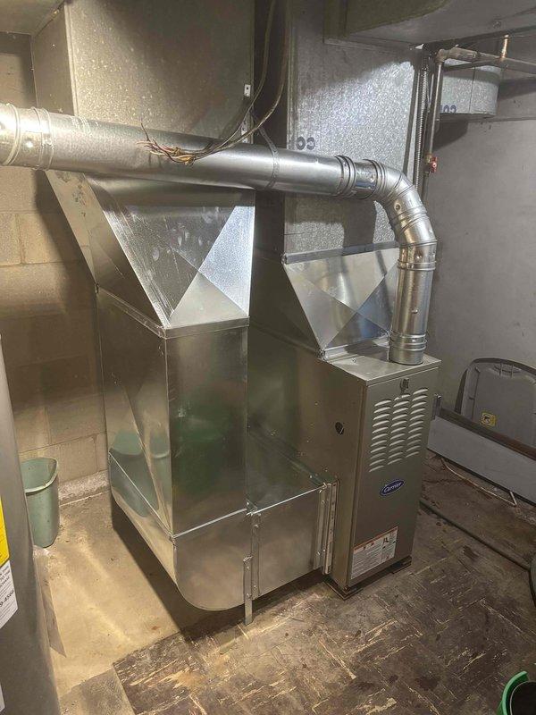 # Furnace Installation Summary

Successfully completed installation of new Carrier furnace unit in basement utility area. Positioned furnace with proper clearances and connected to metal plenum chamber with tapered configuration for optimal airflow distribution. Installed silver metallic ductwork with elbow joint connecting to horizontal trunk line, ensuring proper routing and support throughout the system. Verified all duct connections are sealed and secure to prevent air leakage. Confirmed electrical connections at panel with appropriate circuit protection including fuses and breakers properly rated for equipment load. Tested system startup, verified proper ignition sequence, and confirmed adequate airflow through supply registers. Installation meets all applicable mechanical and electrical code requirements.