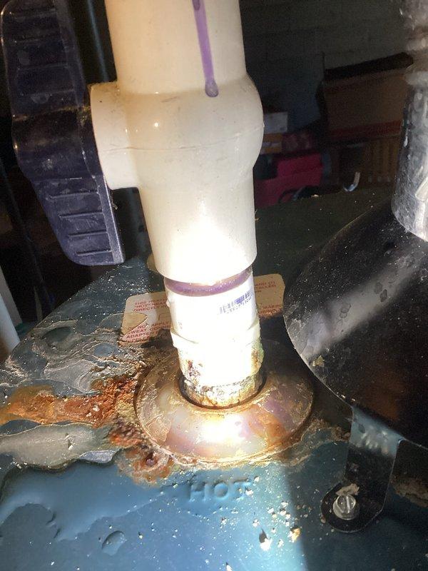 # Plumbing Leak Inspection Report

Responded to service call for leaking pipe investigation. Upon arrival, conducted thorough visual inspection of water heater and associated plumbing connections in utility area. Inspection revealed significant rust and corrosion on water heater top surface, particularly concentrated around pipe connection points. Multiple copper supply lines and galvanized fittings showed signs of age-related deterioration with visible patina and surface oxidation.

Primary concern identified at base of white PVC discharge pipe penetrating through blue metal drip pan. Extensive rust and corrosion present at pipe-to-pan interface, with brown and orange discoloration spreading across metal surface. Water staining and moisture damage visible on surrounding areas, indicating active or recurring leak condition. Rust buildup and textured corrosion patterns suggest prolonged water exposure requiring immediate attention.

Documented conditions with photographs showing water h