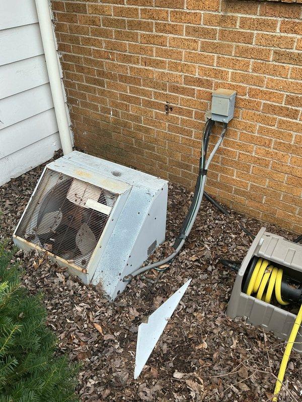 Conducted on-site assessment of existing 52-year-old Luxaire residential HVAC system for complete air conditioning replacement estimate. Evaluated basement-installed furnace and air handler configuration, documenting current gray metal furnace unit with upward-routed white PVC condensate drainage and cylindrical ductwork connections. Inspected outdoor condenser unit mounted on mulch bed against brick exterior wall, noting significant weathering, discoloration, and wear on metal casing consistent with age of system. Photographed both indoor and outdoor equipment to document current installation conditions, equipment specifications, and routing of electrical conduit and drainage lines for replacement planning purposes.