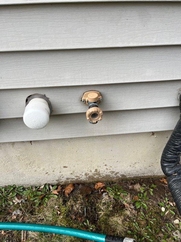 Responded to service call for outdoor faucet with suspected freeze damage after hose was left connected throughout winter season. Upon arrival, inspected dual hose bib installation on exterior wall with vinyl siding. Found one faucet equipped with foam insulation cover while second unit remained exposed. Conducted operational test which revealed active water leak from affected hose bib, confirming freeze damage to internal valve components. 

Documented pre-existing conditions showing water streaming from spout and splashing onto concrete foundation, indicating compromised valve seat or stem assembly due to ice expansion. Verified both faucets for accessibility and assessed extent of damage. One unit showed proper winterization with protective cover in place, while damaged unit exhibited typical failure pattern consistent with water remaining in valve body during freezing temperatures.

Photographed damaged faucet during active leak to document failure mode and surrounding plumbing inf
