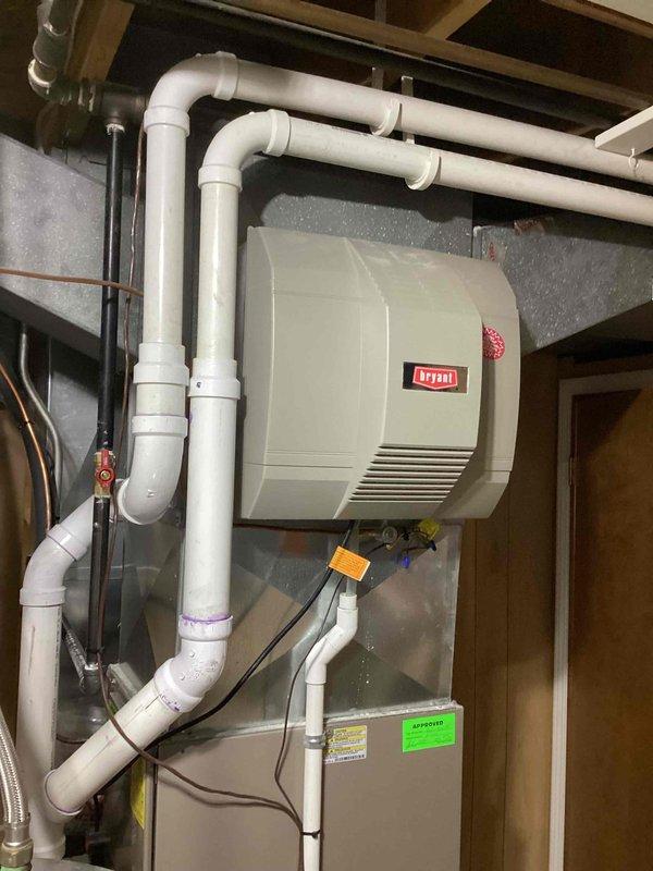 Responded to water leak complaint on 2-year-old Carrier furnace with water accumulating in drain pan. Upon inspection, found condensate drainage system functioning but humidifier experiencing overflow condition. Verified drain lines were clear and properly routed, checked condensate pump operation, and inspected humidifier water feed and drainage connections. Documented equipment configuration and drainage system components with photos for service records.