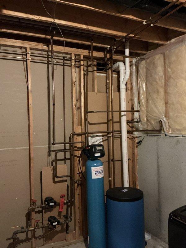 Responded to service call for sump pump drainage pipe leak and water hammer issues affecting multiple fixtures. Upon inspection, identified minor leak in sump pump discharge line where audible dripping occurred during pump cycling. Assessed plumbing system including kitchen sink, dishwasher, and shower connections experiencing aggressive water hammer. Evaluated basement utility area containing sump pump assembly with white PVC discharge piping, water treatment equipment including water softener and pressure tank, and copper supply line distribution system. Documented existing conditions of plumbing infrastructure and mechanical systems for further corrective action recommendations.