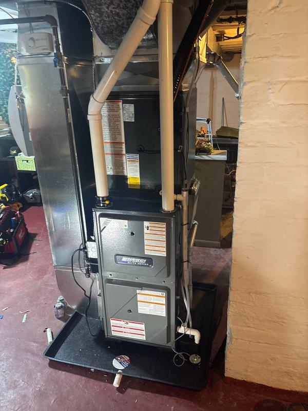 Completed full furnace replacement and new air conditioning system installation at residential property. Installed new gas furnace unit in basement mechanical room with proper venting via white PVC piping, mounted on platform with all required safety labels and specifications clearly visible. Added new outdoor AC condenser unit on concrete pad with electrical disconnect box, conduit run along exterior wall, and refrigerant line set connecting to indoor air handler. All ductwork connections completed, system tested and verified operational.