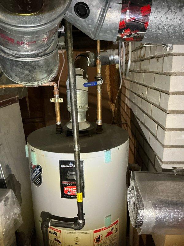 Provided estimate for replacement of existing 20-25 year old Bradford White natural gas tank water heater with new tankless system. Assessed current installation including copper supply lines, blue-handled shutoff valve, and venting configuration in basement utility area. Evaluated electrical requirements for tankless conversion, noting absence of existing electrical infrastructure at installation location and current breaker panel capacity limitations. Documented existing panel with multiple circuits serving furnace, microwave, and lighting loads in unfinished utility space with exposed stud framing. Discussed future electrical upgrade needs including panel amperage increase to accommodate tankless water heater demand, potential EV charger installation, and additional lighting projects. Scheduled follow-up appointment to address electrical scope assessment and provide comprehensive estimate for complete system conversion and electrical infrastructure improvements.