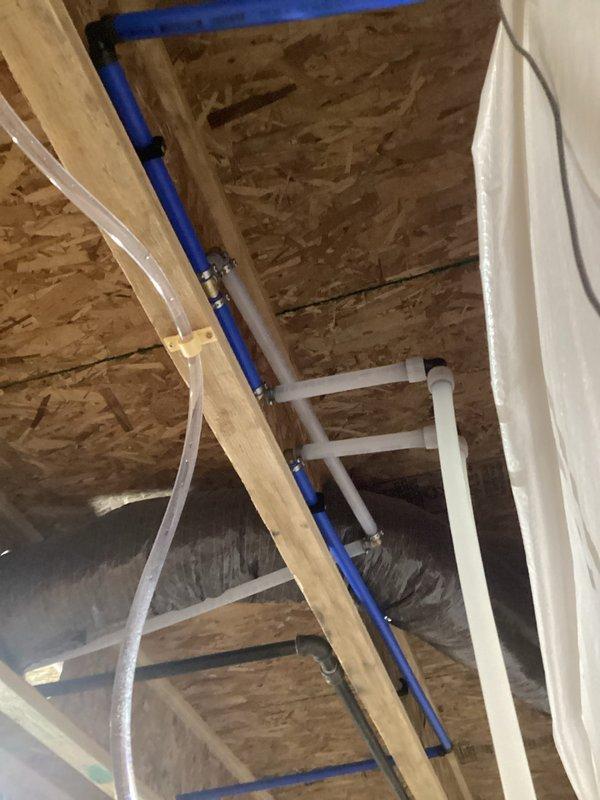 Completed installation of residential water softener system in basement utility area. Installed main white cylindrical softener tank with digital control head and black brine tank for salt storage, positioning equipment against foundation wall with proper drainage access. Ran blue PEX water supply lines from basement through attic space to integrate system with existing plumbing infrastructure, securing all piping with appropriate clips and brackets. Connected system to existing copper/brass valve assembly and installed spigot as specified. All components tested and operational upon completion.