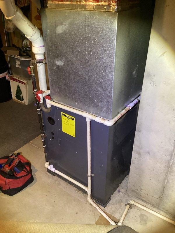Responded to report of furnace leaking water when unit operates. Upon inspection, identified issue with humidifier damper system on 9-year-old Goodman furnace. Examined condensate drainage system including white PVC drain lines and verified proper installation and flow. Inspected Honeywell humidifier unit mounted to furnace cabinet and associated ductwork connections. Documented existing HVAC system configuration including air handler, metal ductwork, and mechanical room setup. Photographed equipment for service records showing unit condition and plumbing connections.