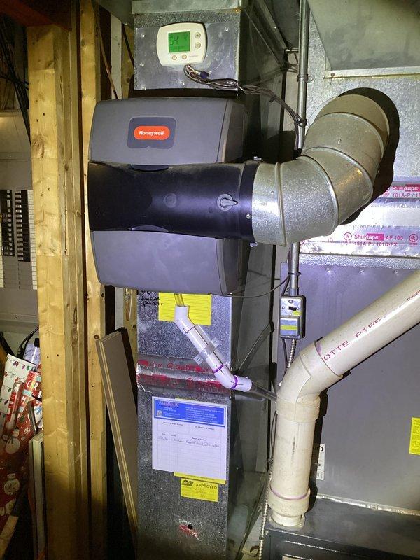 Responded to report of furnace leaking water when unit operates. Upon inspection, identified issue with humidifier damper system on 9-year-old Goodman furnace. Examined condensate drainage system including white PVC drain lines and verified proper installation and flow. Inspected Honeywell humidifier unit mounted to furnace cabinet and associated ductwork connections. Documented existing HVAC system configuration including air handler, metal ductwork, and mechanical room setup. Photographed equipment for service records showing unit condition and plumbing connections.