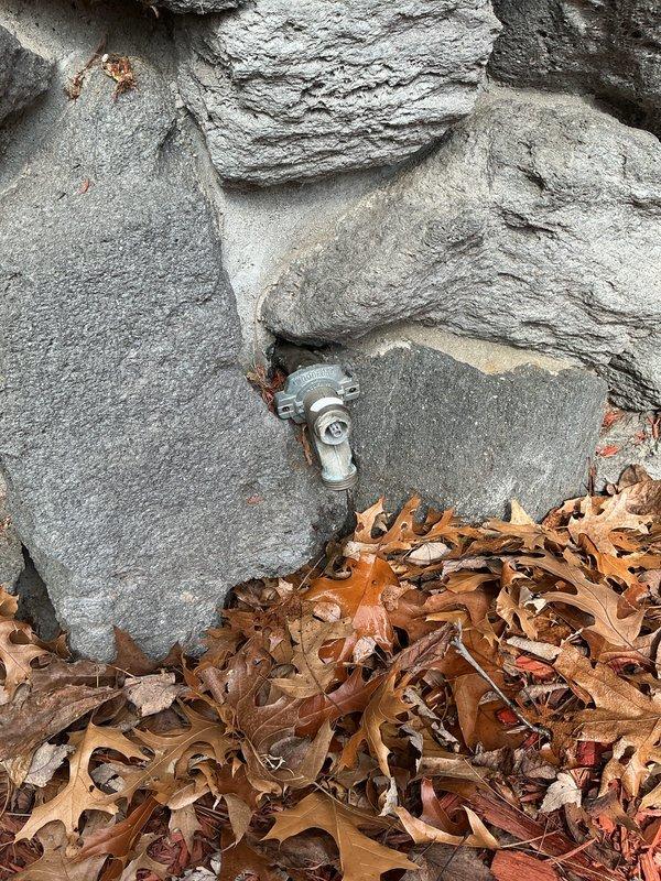 Responded to service call for non-functional exterior faucet with missing handle. Upon arrival, located galvanized steel spigot protruding from stone foundation at ground level, surrounded by accumulated leaf debris. Assessed exterior hose bib assembly and determined handle mechanism was absent, preventing water control. Accessed interior plumbing connections through basement utility area to verify supply line integrity and shut-off valve functionality. Replaced defective exterior faucet assembly with frost-proof sillcock, ensuring proper installation through foundation wall and secure mounting to prevent future damage. Tested water flow and verified complete shut-off capability of new handle assembly.
