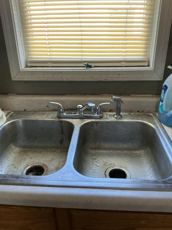 Installed customer-supplied kitchen faucet at double-basin stainless steel sink, replacing existing corroded fixture with extensive rust staining around base and mounting hardware. Cleared backed-up toilet affecting single fixture; restored proper drainage and flushing function without requiring toilet replacement.