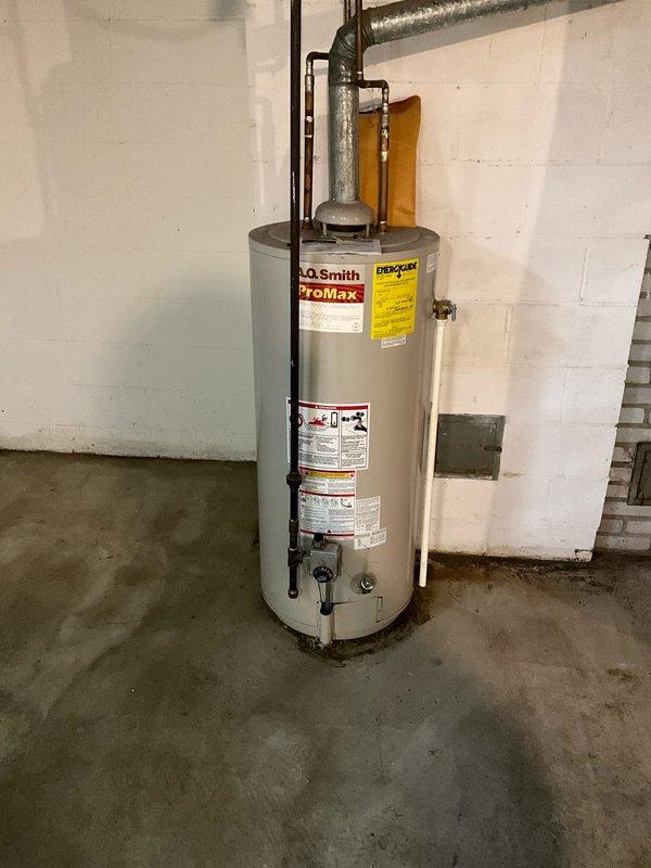 Provided estimate for water heater replacement in residential basement utility room. Evaluated existing A.O. Smith ProMax water heater installation, documented current plumbing connections including galvanized venting system with elbow joint configuration, assessed condition of concrete floor showing moisture staining around base of unit, and photographed all equipment specifications and surrounding utility infrastructure to prepare comprehensive replacement proposal.