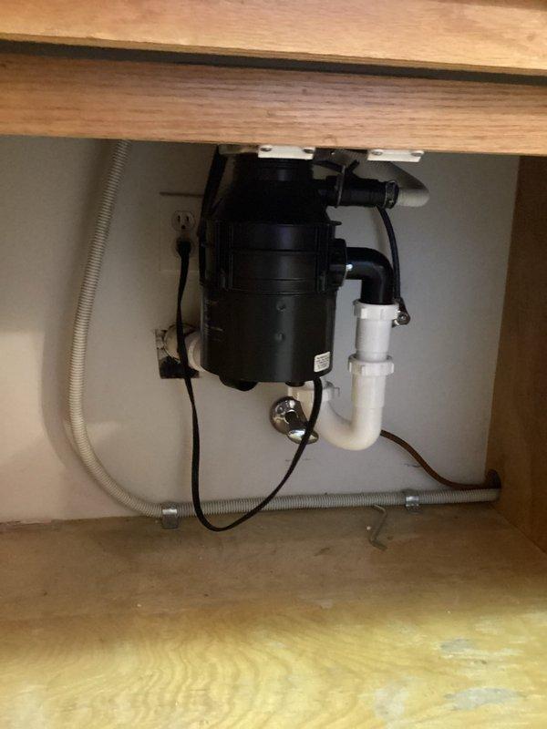 Installed new garbage disposal unit under kitchen sink with complete drain assembly replacement. Connected disposal to existing electrical outlet and integrated dishwasher drain line into system. Configured white PVC P-trap assembly to ensure proper drainage and venting. All plumbing connections secured and tested for leaks, with disposal unit properly mounted to sink basin using standard mounting hardware.