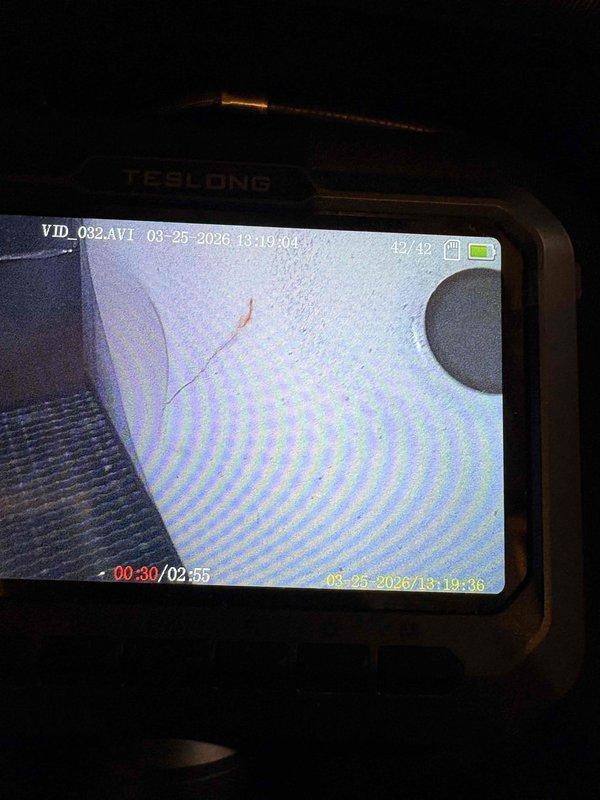 Responded to service call for water leaking from 20-year-old Lennox furnace. Upon inspection, utilized borescope camera to examine internal ductwork and drainage pathways for blockages or damage. Identified water staining and corrosion at pipe penetration point on wall, indicating active leak from condensate drain system. Documented conditions with photos showing rust streaking down wall surface and connection hardware requiring attention. Condensate drainage components inspected including drain lines and pump assembly with attached hoses.