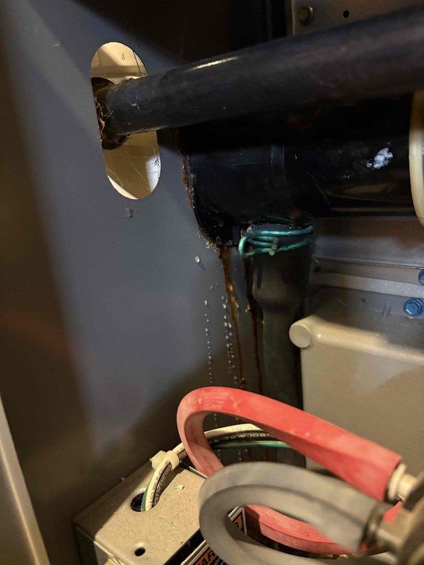 Responded to service call for water leaking from 20-year-old Lennox furnace. Upon inspection, utilized borescope camera to examine internal ductwork and drainage pathways for blockages or damage. Identified water staining and corrosion at pipe penetration point on wall, indicating active leak from condensate drain system. Documented conditions with photos showing rust streaking down wall surface and connection hardware requiring attention. Condensate drainage components inspected including drain lines and pump assembly with attached hoses.