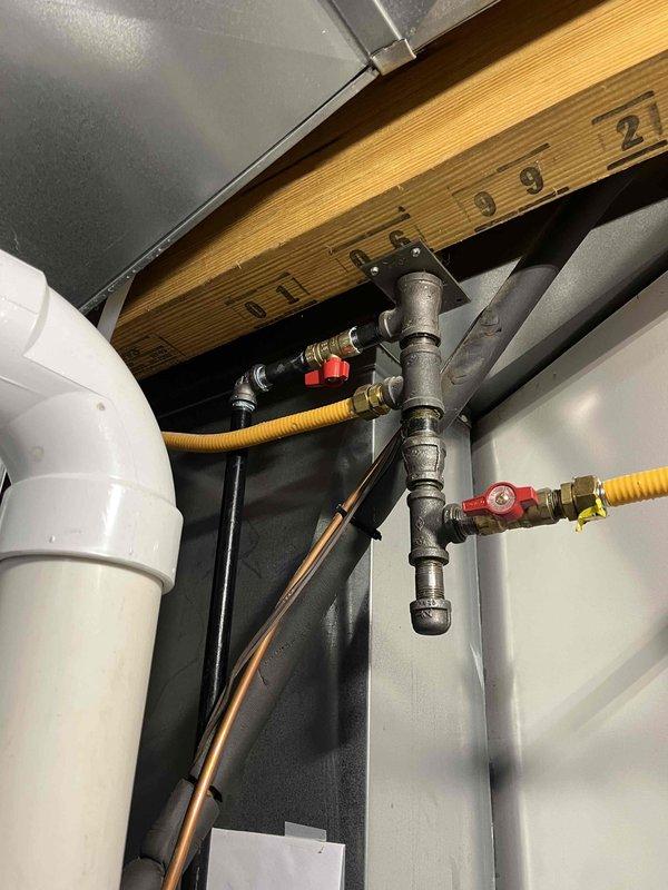 Completed full furnace installation in residential utility space. Installed new two-stage forced-air furnace unit with proper venting system utilizing white PVC piping with appropriate elbows and connections. Connected yellow flexible gas lines (CSST) to furnace with brass fittings and red-handled shut-off valves for safety and code compliance. Positioned unit on black drain pan for condensate management with black flexible drainage line routed to proper discharge point. Installed electrical panel/air handler unit adjacent to furnace with all required labeling and specifications clearly visible. Secured all copper tubing and gas lines with proper mounting brackets along wall surfaces. Verified all connections for gas-tight integrity and proper ventilation exhaust. System tested and operational upon completion.