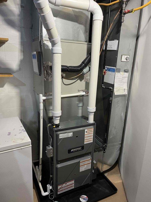 Completed full furnace installation in residential utility space. Installed new two-stage forced-air furnace unit with proper venting system utilizing white PVC piping with appropriate elbows and connections. Connected yellow flexible gas lines (CSST) to furnace with brass fittings and red-handled shut-off valves for safety and code compliance. Positioned unit on black drain pan for condensate management with black flexible drainage line routed to proper discharge point. Installed electrical panel/air handler unit adjacent to furnace with all required labeling and specifications clearly visible. Secured all copper tubing and gas lines with proper mounting brackets along wall surfaces. Verified all connections for gas-tight integrity and proper ventilation exhaust. System tested and operational upon completion.