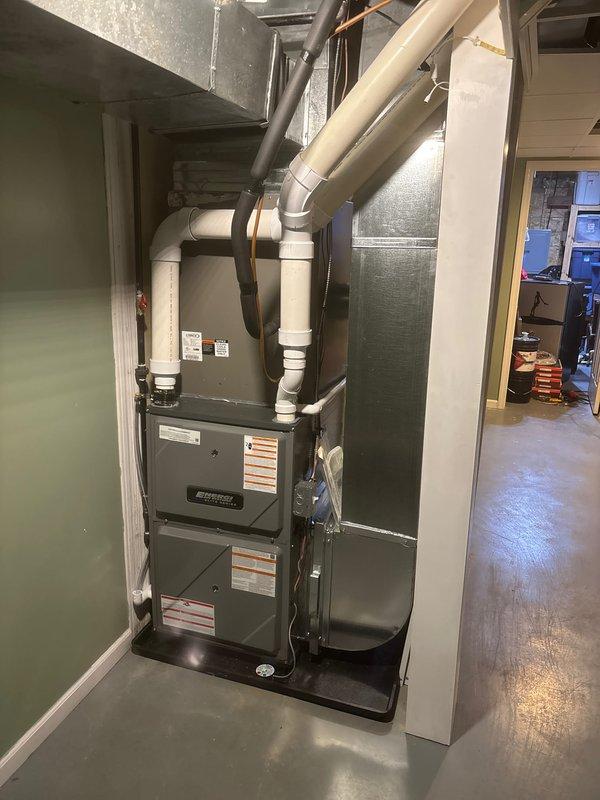 Completed full furnace replacement in residential basement utility room. Installed new gray metal furnace unit with proper ventilation routing using white PVC piping, configured ductwork connections, and positioned unit on drain pan for condensate management. System installed adjacent to existing water heater with all components properly secured, vented, and tested for operational functionality.