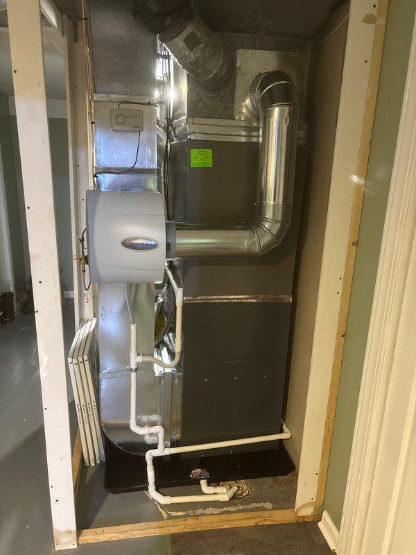 Completed full furnace replacement in residential basement utility room. Installed new gray metal furnace unit with proper ventilation routing using white PVC piping, configured ductwork connections, and positioned unit on drain pan for condensate management. System installed adjacent to existing water heater with all components properly secured, vented, and tested for operational functionality.