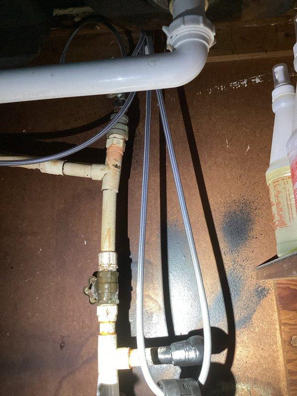 Responded to kitchen sink leak in 1959-built home. Upon inspection, found deteriorated supply line connections and aging plumbing components beneath sink cabinet. Replaced compromised supply lines with new braided stainless steel flex hoses, installed new shutoff valve with brass fittings, and updated worn pipe connections. Removed old discolored copper and brass sections showing significant patina and corrosion. Verified all connections for proper seal, tested system under pressure, and confirmed leak resolution with no active dripping or moisture present.