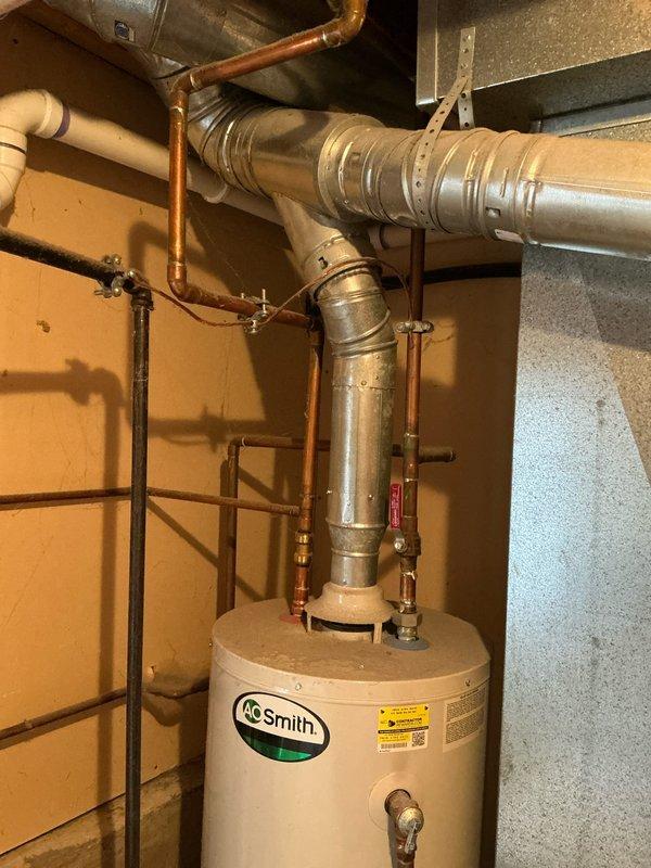 Provided estimate for replacement of original 2006 A.O. Smith water heater that has reached end of serviceable life at 20 years old. Documented existing installation including copper supply lines, galvanized metal flue pipe, and current positioning in basement utility area for accurate replacement specifications.