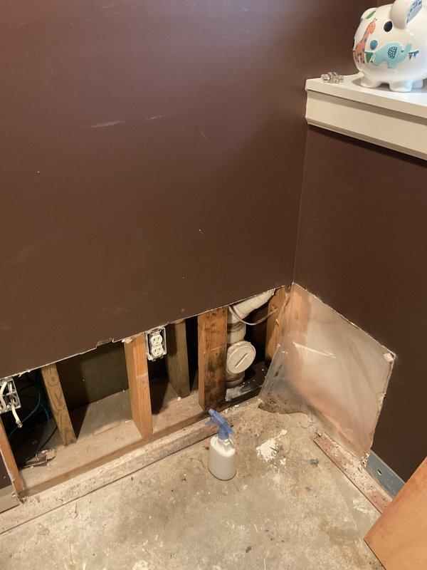 Responded to plumbing leak emergency and performed exploratory drywall removal to locate source of water intrusion. Upon opening wall cavity, exposed vertical PVC plumbing line and installed pressure gauge for leak detection and monitoring. Documented findings with photographs showing exposed wall framing, plumbing components, and extent of water damage to drywall and baseboard materials for insurance and repair planning purposes.