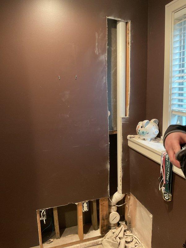 Responded to plumbing leak emergency and performed exploratory drywall removal to locate source of water intrusion. Upon opening wall cavity, exposed vertical PVC plumbing line and installed pressure gauge for leak detection and monitoring. Documented findings with photographs showing exposed wall framing, plumbing components, and extent of water damage to drywall and baseboard materials for insurance and repair planning purposes.