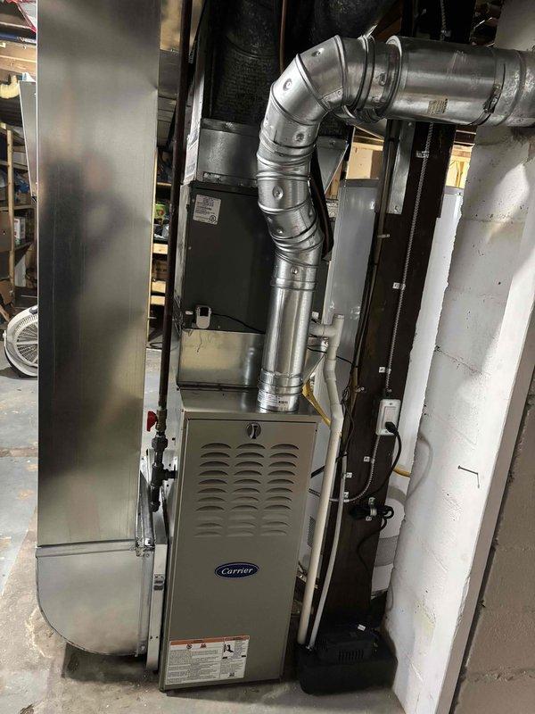 Completed full residential furnace installation featuring a new Carrier brand heating unit in basement utility area. System includes comprehensive ductwork routing with metallic segmented construction, multiple elbow joints, and proper ventilation connections to distribute conditioned air throughout the residence. All electrical connections, wiring, and mechanical components installed to manufacturer specifications and code requirements. Unit positioned on concrete floor with complete duct network integrated into existing infrastructure. System tested, activated, and confirmed operational.