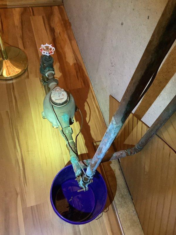 Responded to utility closet leak at main water service entry point. Upon arrival, found heavily corroded galvanized steel piping with significant rust deterioration and failing connections at the main shutoff valve assembly. The existing plumbing showed extensive oxidation with compromised fittings and threading, indicating long-term moisture exposure and age-related failure. Assessed the main valve assembly with pressure gauge and determined the leak was originating from corroded pipe joints near the water meter connection. Due to advanced corrosion throughout the affected section and customer's upcoming flooring installation, recommended addressing the leak immediately to prevent further water damage. Positioned collection bucket to contain any residual water during inspection and documented the condition of all visible components for repair planning.