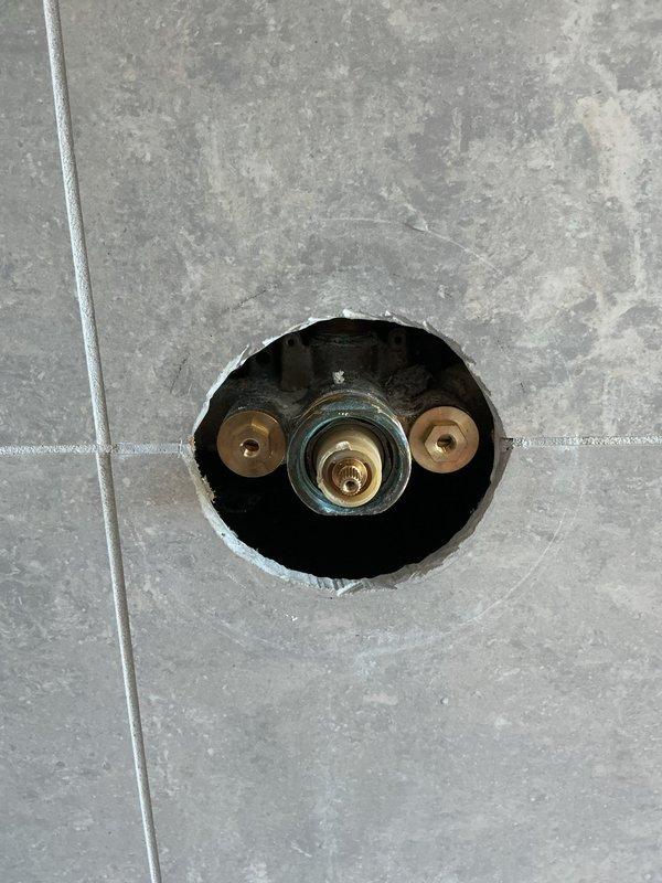 Responded to recurring shower valve issue where cartridge was causing the same malfunction as previous service call. Accessed valve assembly through existing wall opening in tiled shower enclosure and inspected brass mounting flanges and central valve stem mechanism. Completed no-charge warranty repair to resolve persistent cartridge defect.