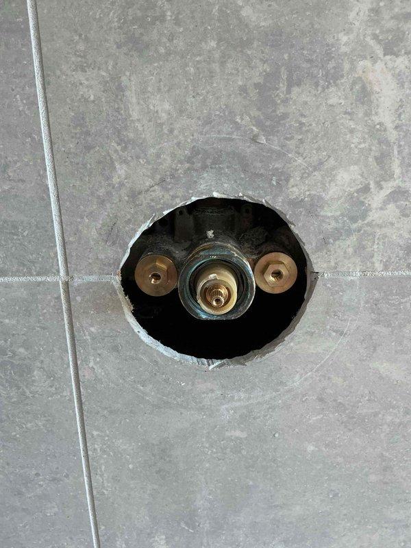Responded to recurring shower valve issue where cartridge was causing the same malfunction as previous service call. Accessed valve assembly through existing wall opening in tiled shower enclosure and inspected brass mounting flanges and central valve stem mechanism. Completed no-charge warranty repair to resolve persistent cartridge defect.
