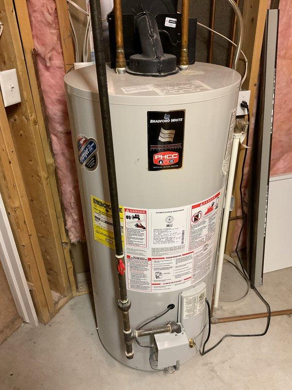 Conducted on-site water heater estimate for residential property. Evaluated existing Bradford White water heater installation in basement utility area, documenting current unit configuration, plumbing connections including copper hot and cold water lines with brass fittings, draft hood assembly, and surrounding mechanical systems. Assessed installation location within framed wall space with proper clearances, photographed existing conditions including PVC venting, electrical connections, and overall system layout to provide accurate replacement estimate.