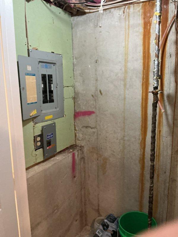Conducted electrical estimate for replacement of original 1970s electrical panel in basement of single-family home with two failed circuit breakers. Inspected existing gray panel box mounted on light green painted concrete wall in unfinished basement area, documented deteriorated breakers and overall panel condition. Assessed installation requirements including access to service entrance, existing conduit routing through exposed ceiling joists, and connection points to exterior meter box with white PVC conduit runs. Photographed current electrical infrastructure to provide comprehensive replacement quote for full panel upgrade to meet current code requirements and restore safe electrical service to affected circuits.
