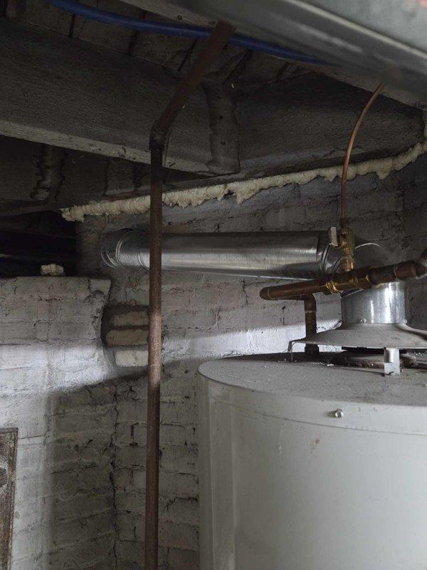 Responded to service call for non-functioning water heater approximately fifteen years old. Upon arrival, accessed utility area via back entrance as requested. Performed visual inspection of existing water heater unit and surrounding plumbing infrastructure. Documented condition of 15-year-old residential water heater, associated copper piping, brass fittings, pressure relief valve assembly, and connection points. Observed aged plumbing components with oxidation present on copper lines and galvanized steel piping. Photographed existing installation including top-mounted plumbing connections, PEX supply lines, and ventilation ductwork for reference. Provided estimate for complete water heater replacement as requested.